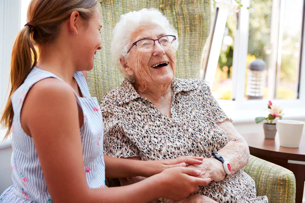 Senior Woman Sitting In A Chair Laughing With Young Family Member