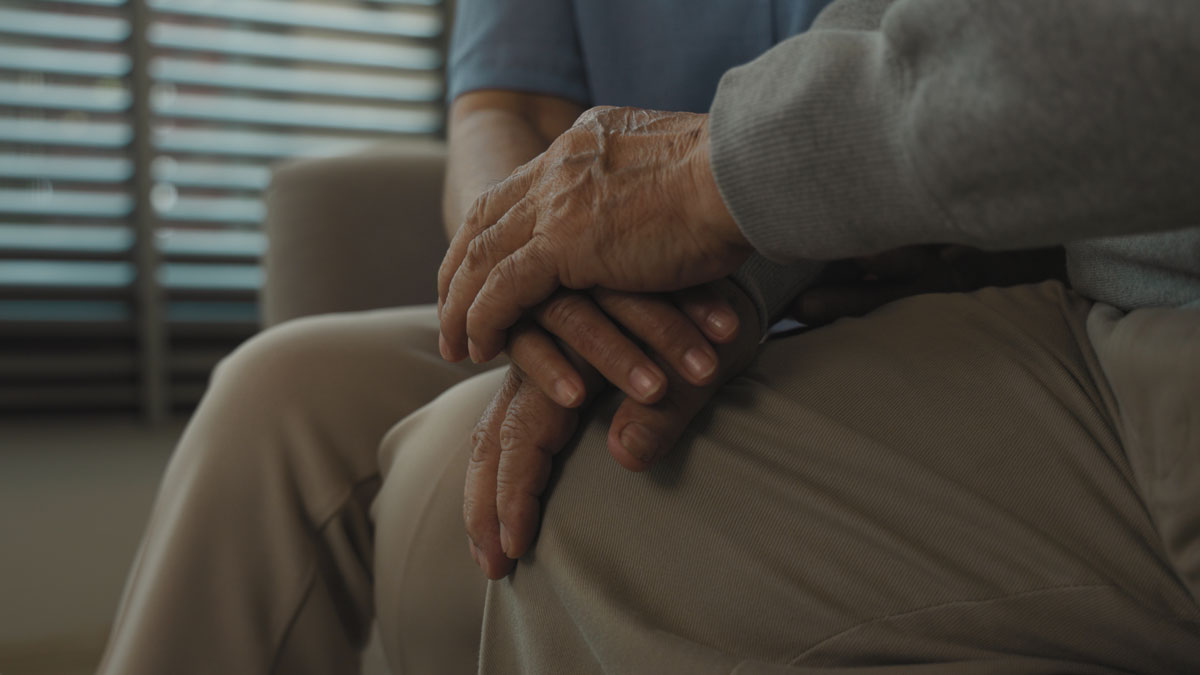 Close-up of a senior woman comforting hand as holds the hand of a sad elderly man