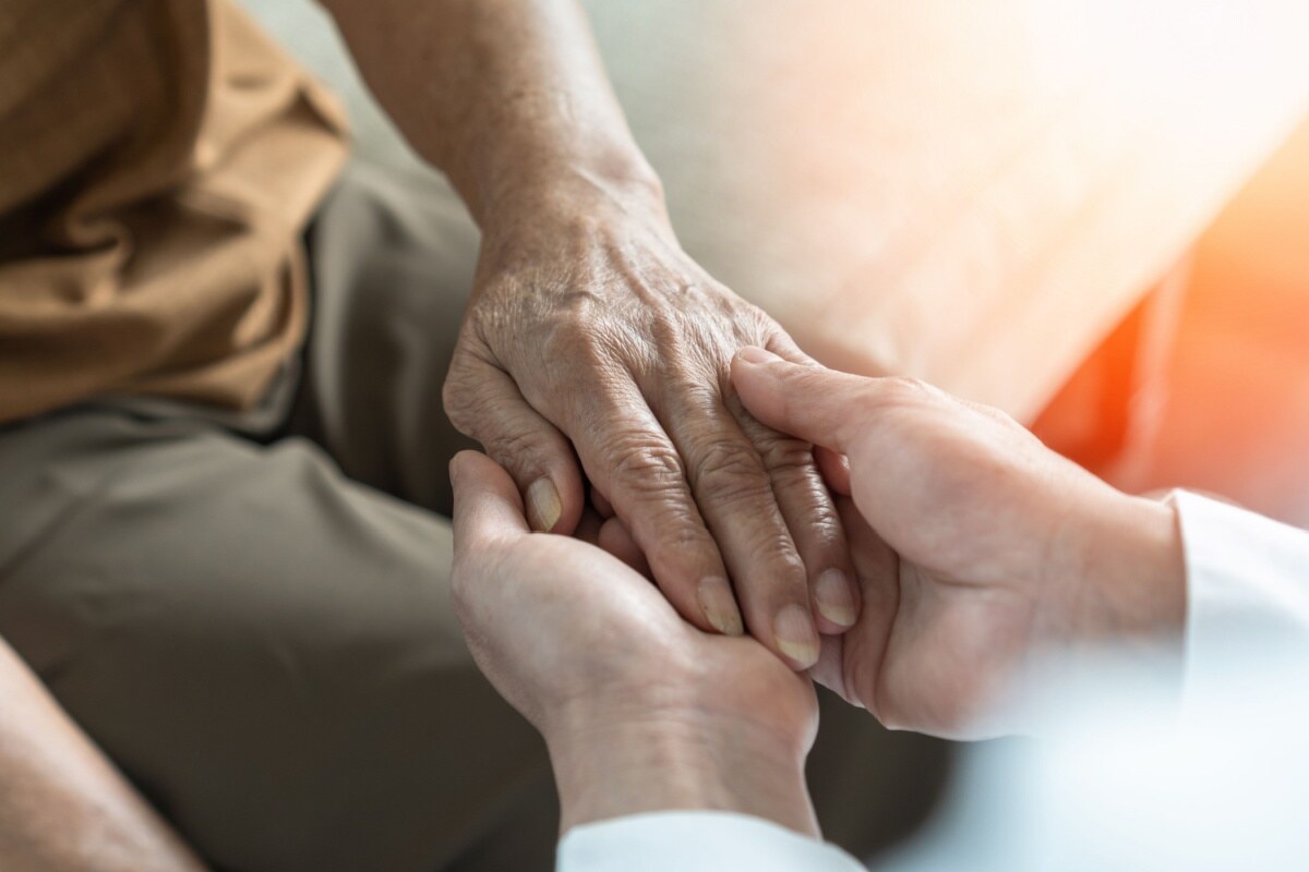 Elderly person’s hand in the hands of a medical caregiver.
